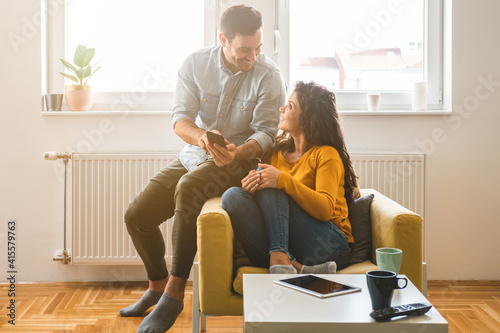 Smiling couple looking in smartphone together at home. Beautiful loving couple laughing and watching something on mobile phone