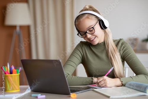 Cheerful school girl having online lesson, using laptop at home