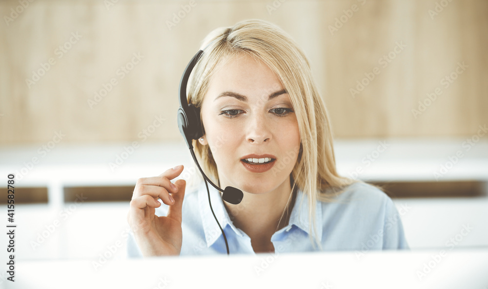 Blonde business woman sitting and communicated by headset in call center office. Concept of telesales business or home office occupation Blonde business woman sitting and communicated by headset in call center office. Concept of telesales business or home office occupation