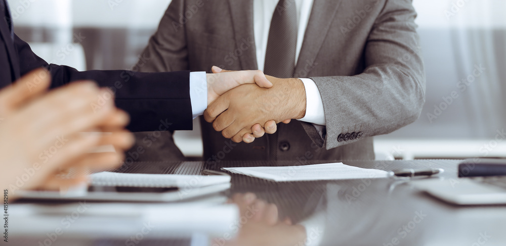 Unknown business people are shaking hands after contract signing in modern office, close-up. Handshake as successful negotiation ending