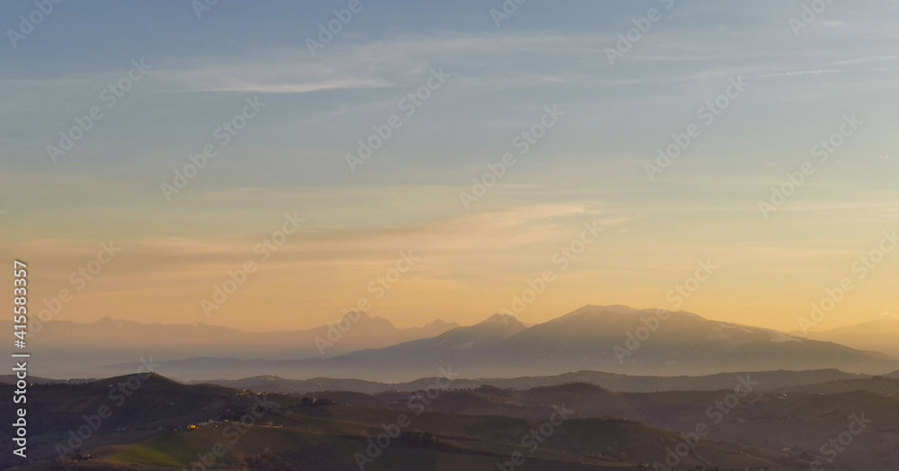 Montagne e valli dell’Appennino in un tramonto di luce e foschia azzurro e arancio