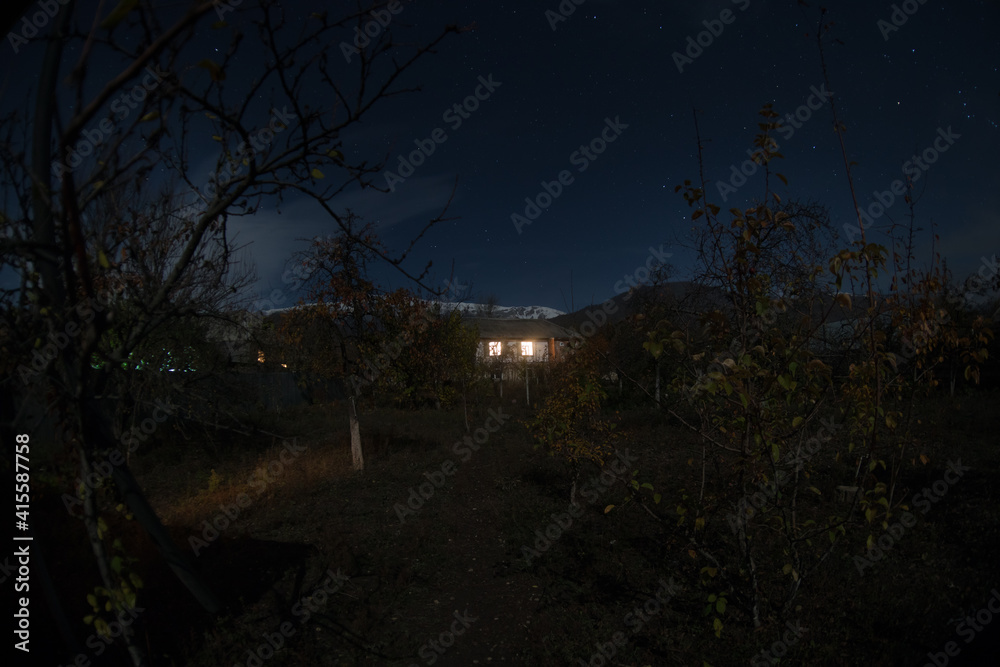 Fototapeta premium Mountain night landscape of building at forest at night with moon or vintage country house at night with clouds and stars. Summer night.