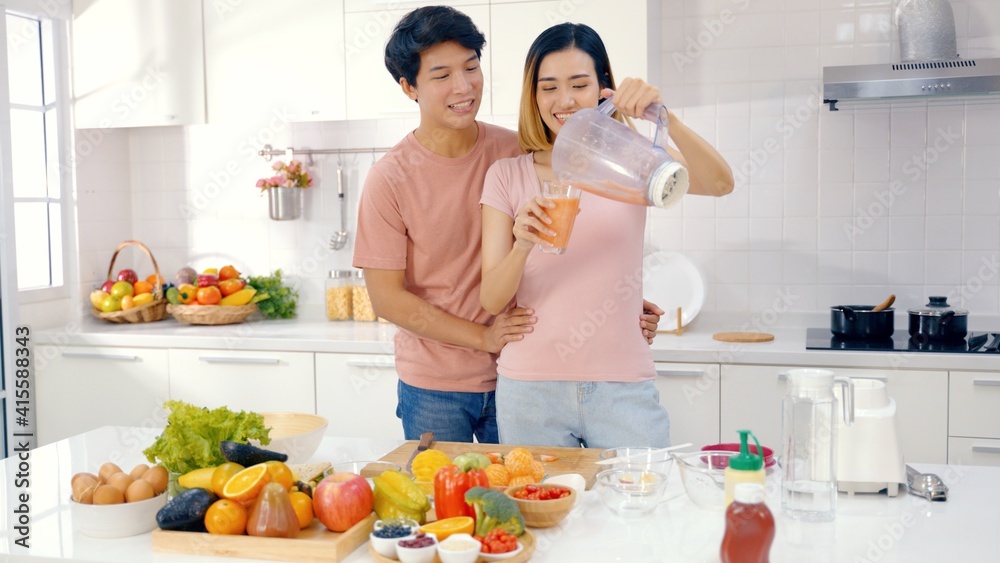 Asian couple feed each other while cooking together in modern kitchen enjoy conversation and healthy vegetarian salad food preparation. Lifestyle, happy homeowners, romantic date, hobby, love concept.