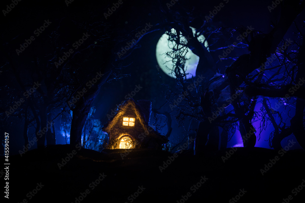 Fototapeta premium Old house with a Ghost in the forest at night or Abandoned Haunted Horror House in fog. Old mystic building in dead tree forest. Trees at night with moon. Surreal lights. Horror Halloween concept