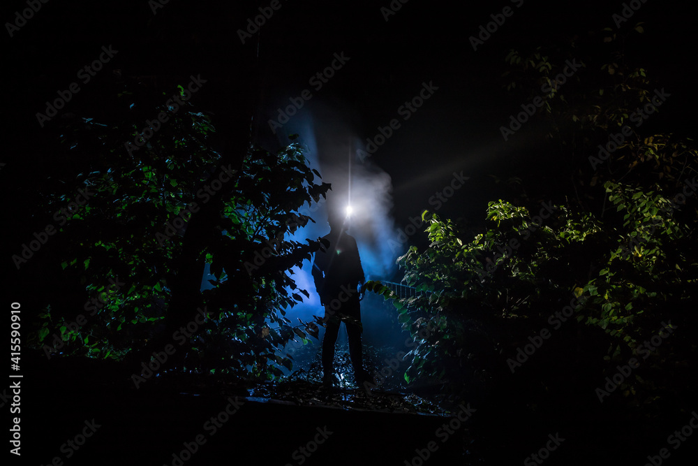Obraz premium strange light in a dark forest at night. Silhouette of person standing in the dark forest with light. Horror halloween concept. strange silhouette in a dark spooky forest at night