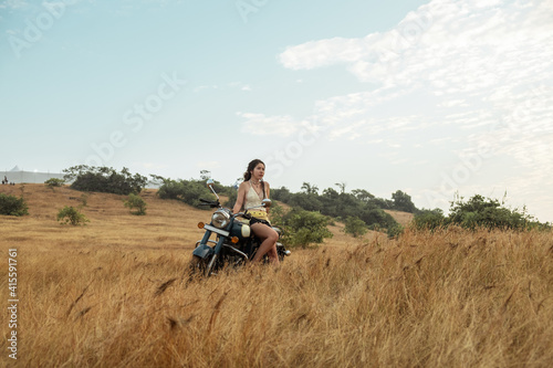 A woman sits on a motorcycle in a field