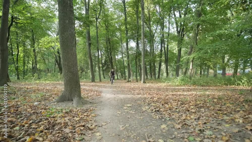 Front view of man on bicycle with glasses riding away in the forest road. Man on a mountain bike rides through the forest in summer sunrise. Front view of man on bicycle with glasses riding away in the forest road. Man on a mountain bike rides through the forest in summer sunrise.