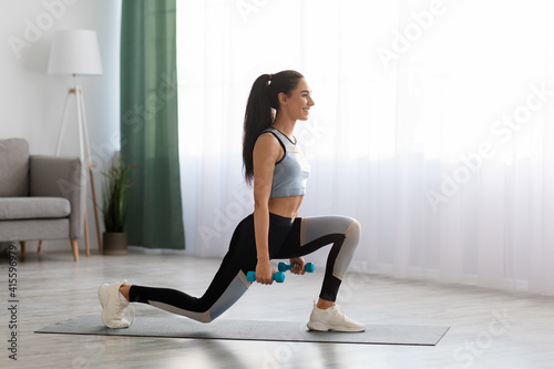 Sporty young woman doing lunges with dumbbells at home