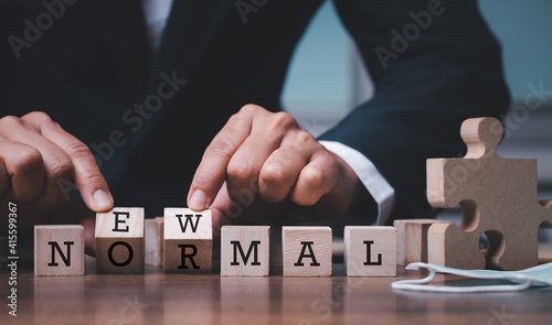 Businessman hand flipping wooden cubes with NEW NORMAL word and mask.