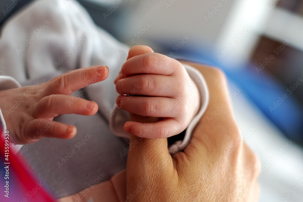 Die Hand eines Neugeborenen greift einen Finger der Mutter während es die andere Hand nach ihr ausstreckt

