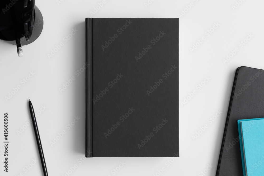 Black book mockup with workspace accessories on the white table. Black book mockup with workspace accessories on the white table.