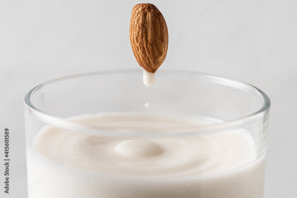 Ταπετσαρία Almond milk drop flowing from the whole nut into the glass full of plant based milk