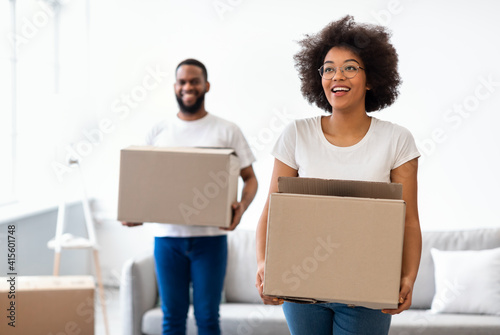 Joyful Black Spouses Carrying Moving Boxes Entering New Home Together
