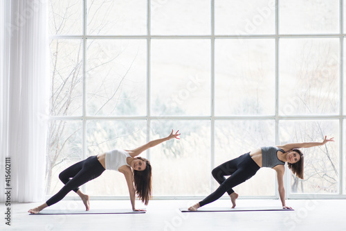 Two beautiful women performing synchronised yoga in a modern studio