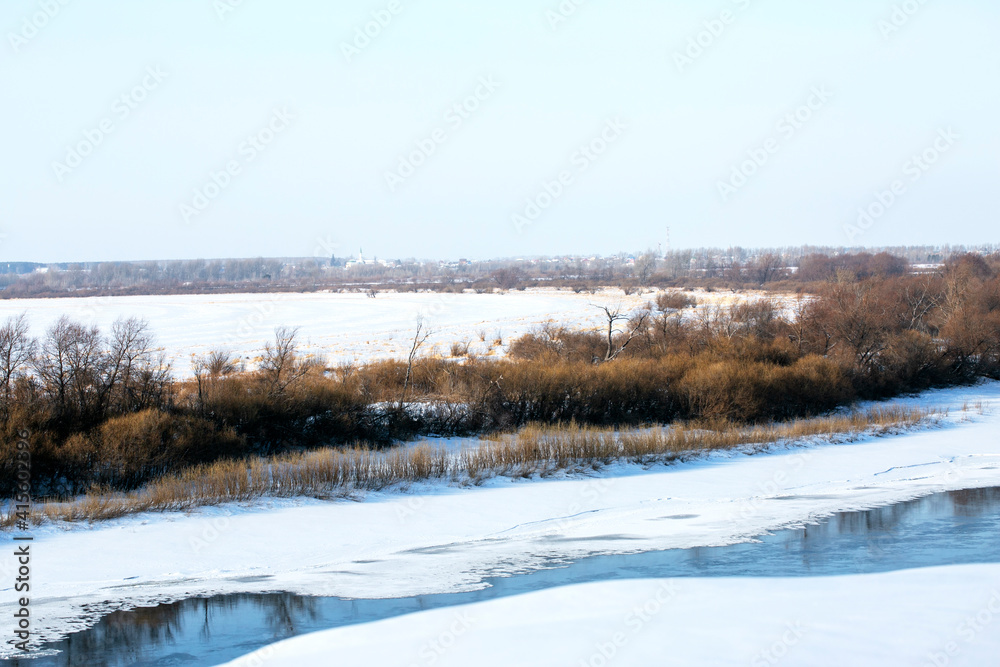 Winter landscape of a forest lake. Beautiful winter landscape scene background with snowy trees and icy river. Frosty winter beauty