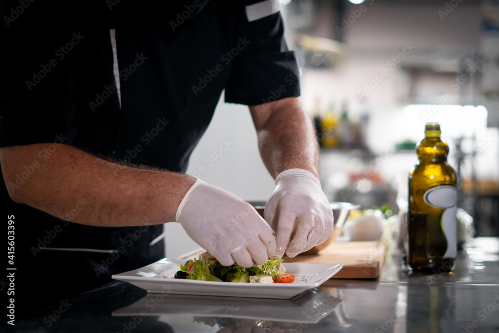 chef cook hands in gloves prepare or put healthy greek salad on plate at kitchen chef cook hands in gloves prepare or put healthy greek salad on plate at kitchen