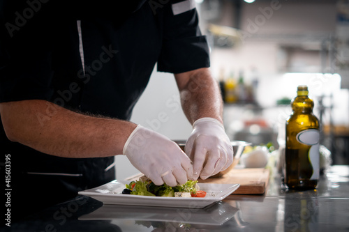 Fototapeta Naklejka Na Ścianę i Meble -  chef cook hands in gloves prepare or put healthy greek salad on plate at kitchen