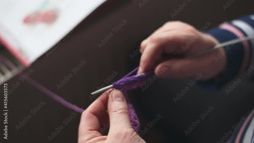 close up of woman knitting with purple whool at home to create a doll. focus on knitting needle close up of woman knitting with purple whool at home to create a doll. focus on knitting needle
