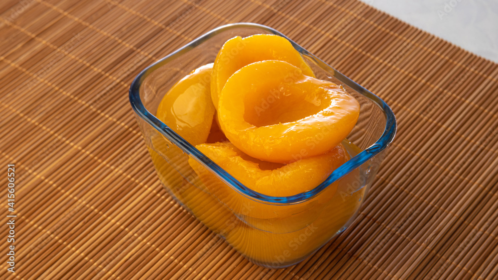 Peaches in syrup placed in glass bowl on wooden mat, gray gradient background, selective focus.