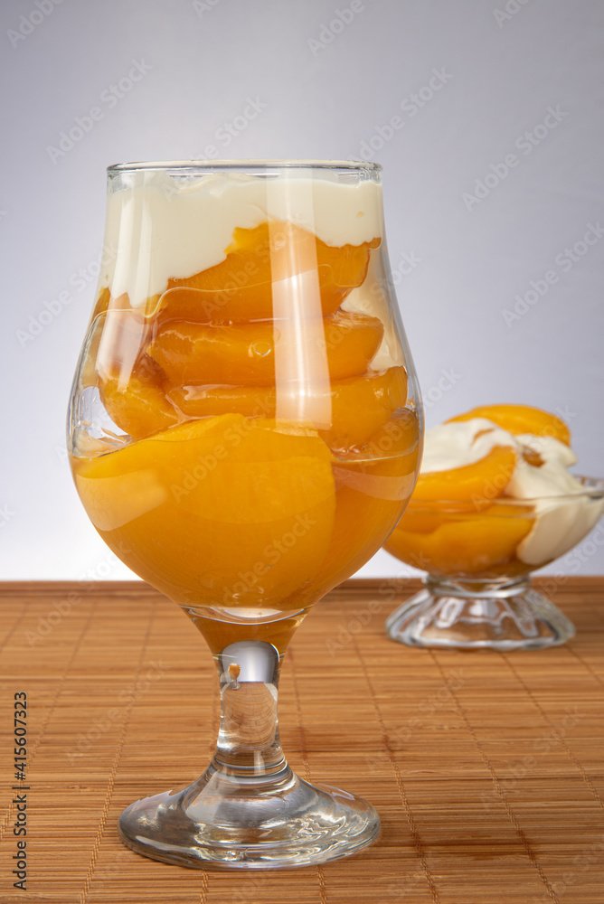 Peaches in syrup placed in two bowls covered with sour cream on wooden mat, gray gradient background, selective focus. Peaches in syrup placed in two bowls covered with sour cream on wooden mat, gray gradient background, selective focus.