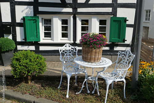 Closeup of a white squiggly metal table with chairs in front of a beautiful timber framed house in Hilden, Germany, Europe
