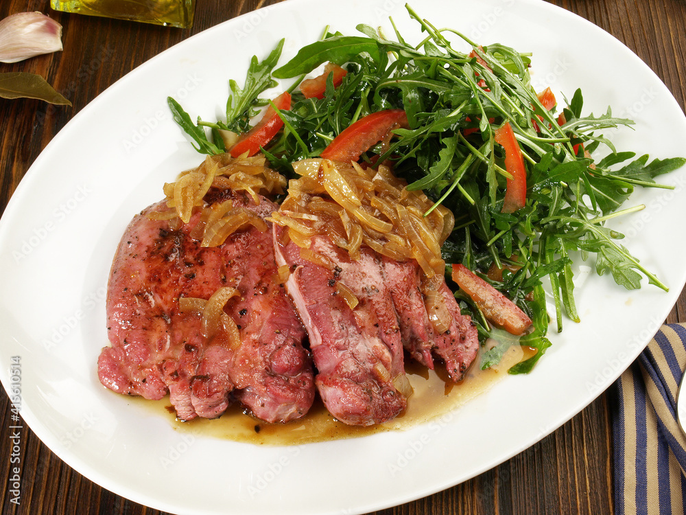 Roasted Veal Tongue Meat Slices with roasted Onions and Salad on wooden Background Roasted Veal Tongue Meat Slices with roasted Onions and Salad on wooden Background