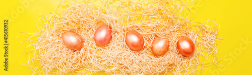 Colored pink and orange eggs on hay over yellow color, bright easter background photo