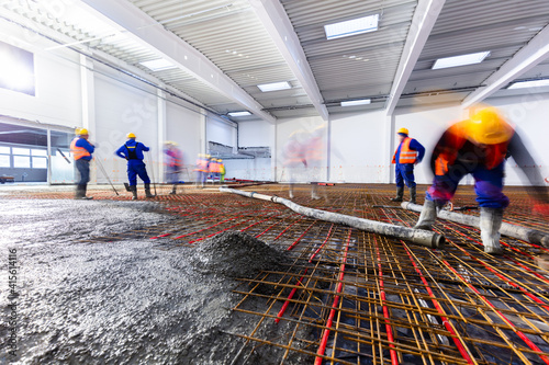 Workers do concrete screed on floor with heating in a new warehouse building photo