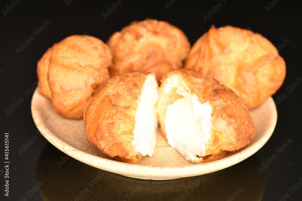 Tasty chouquettes with cream on a saucer, on a black background. Tasty chouquettes with cream on a saucer, on a black background.