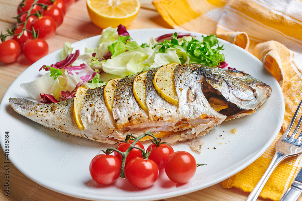 Tasty grilled dorado fish with lemons and herbs served on the plate with tomatoes and salad. Close up view. Tasty grilled dorado fish with lemons and herbs served on the plate with tomatoes and salad. Close up view.