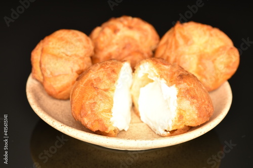 Tasty chouquettes with cream on a saucer, on a black background.