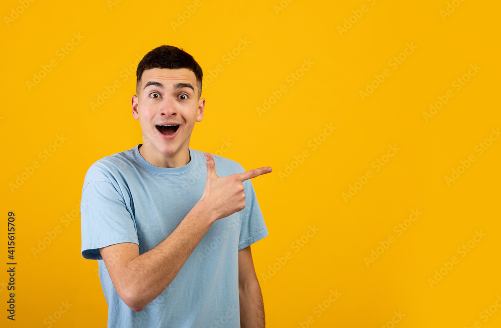 Excited young guy opening mouth in shock and pointing aside at blank space on orange studio background, banner design Excited young guy opening mouth in shock and pointing aside at blank space on orange studio background, banner design