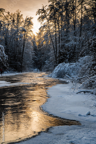 The wild frozen small river in the winter wood, the wild nature at sunset, the river of red color, ice, snow-covered trees