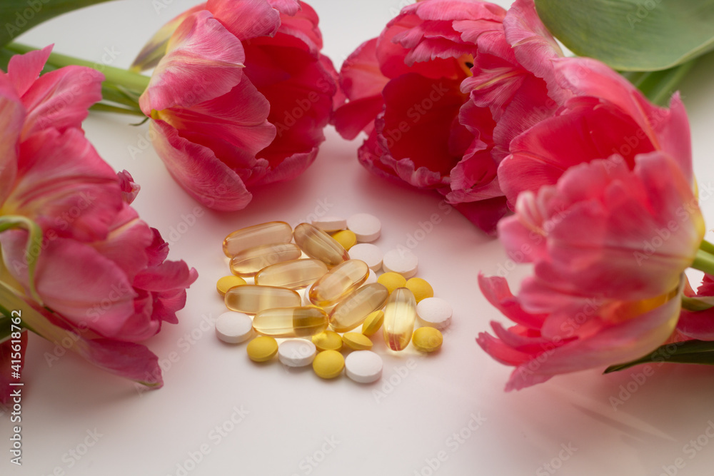 Obraz premium Concept of supplementation for spring. Closeup of vitamin D, zinc and vitamin C pills surrounded by flowers.