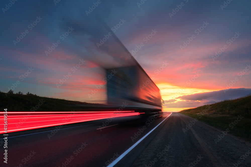 Motion blur. A large truck is driving along the highway at high speed. Sky with bright red clouds. Delivery of cargo. - obrazy, fototapety, plakaty 