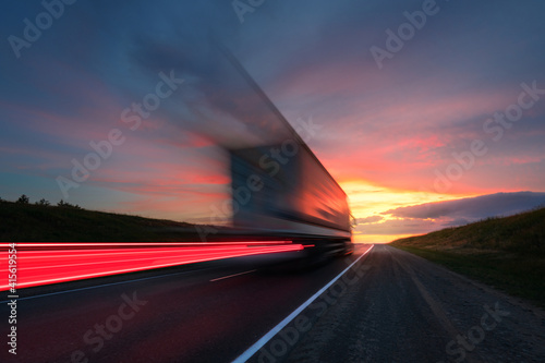Motion blur. A large truck is driving along the highway at high speed. Sky with bright red clouds. Delivery of cargo.