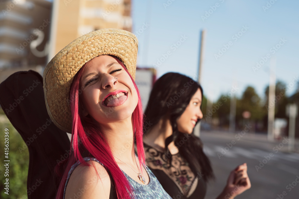 beautiful woman in hat and pink hair sticks her tongue out at camera in outdoor portrait