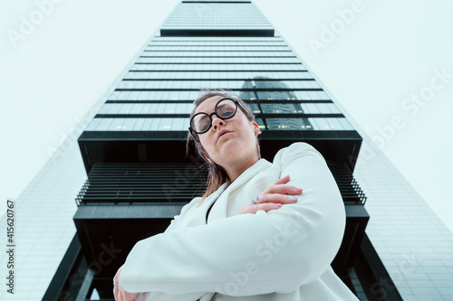 Caucasian woman with formal jacket and nerdy glasses, with a serious and arrogant expression, with an skyscraper in the background. Job, economy, companies, businesswoman and students concept.