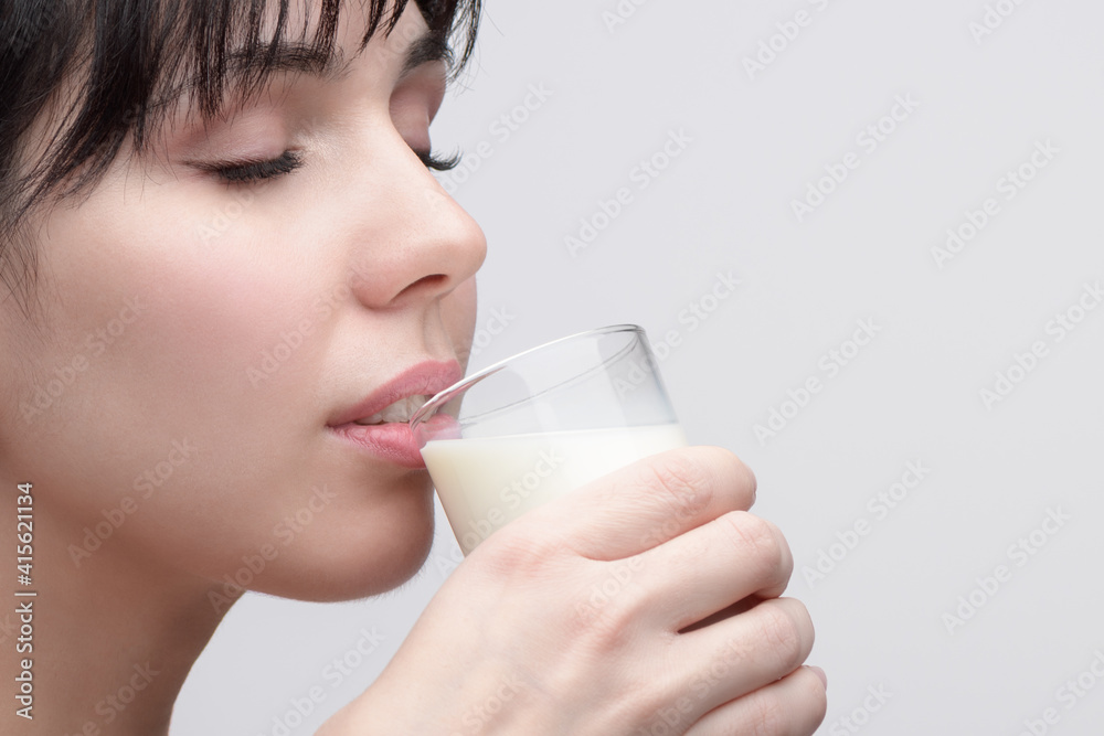 closeup Portrait of young beautiful woman with closed eyes drinking milk from a transparent glass closeup Portrait of young beautiful woman with closed eyes drinking milk from a transparent glass
