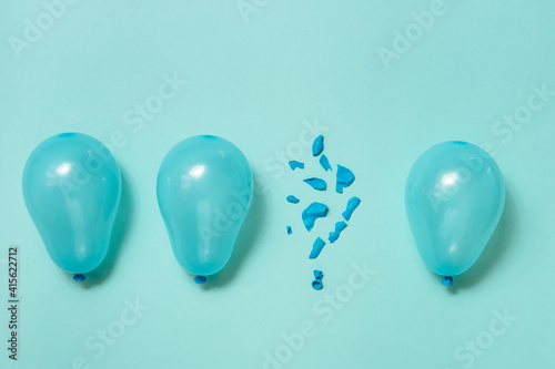 One popped balloon among other whole blue balloons on blue background. Burnout or being under pressure concept. Top view flat lay.