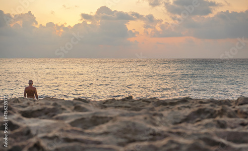 Sand on beach, closeup low angle detail, person seen from behind in background ready for morning swim, orange pink sunrise sky background