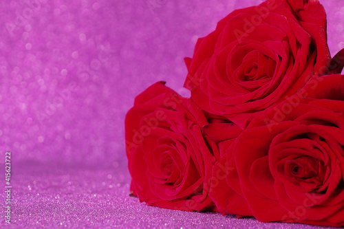 three red roses on purple shiny background. copy space. © Olga