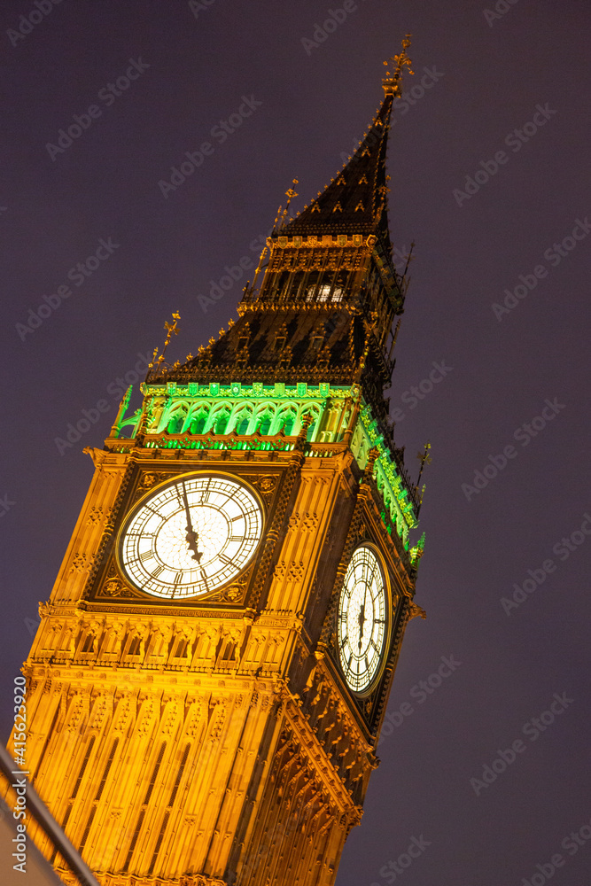 Big Ben clock face illuminated at night with dark skies behind with orange and green lights on the clock of Elizabeth Tower next to the Houses of Parliament in Westminster,, London, England - obrazy, fototapety, plakaty 