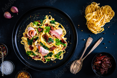 Tableau sur toile Tagliatelle with bacon, sun-dried tomatoes and spinach in alfredo sauce on black