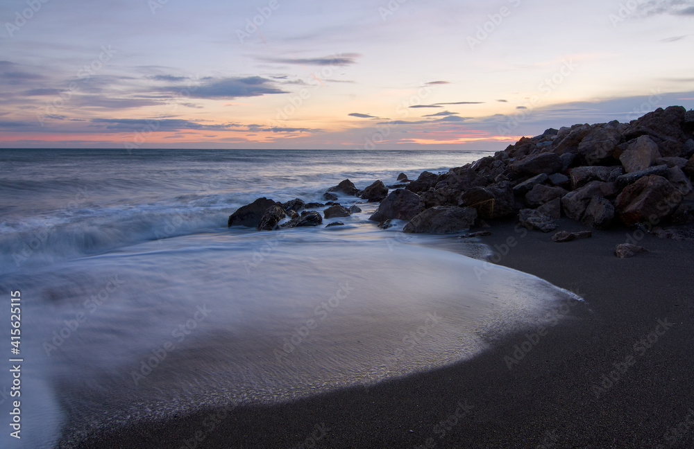 Obraz premium A picturesque scene of the sunset above sea waters seen through the rocky shore