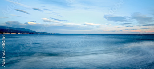 A panoramic shot of a wavy blue sea under a bluish sky