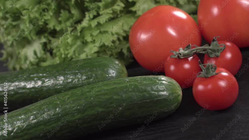 tasty green cucumbers and red tomatoes and cherry tomatoes and lettuce rotating on black wooden table close up view from top. tasty green cucumbers and red tomatoes and cherry tomatoes and lettuce rotating on black wooden table close up view from top.