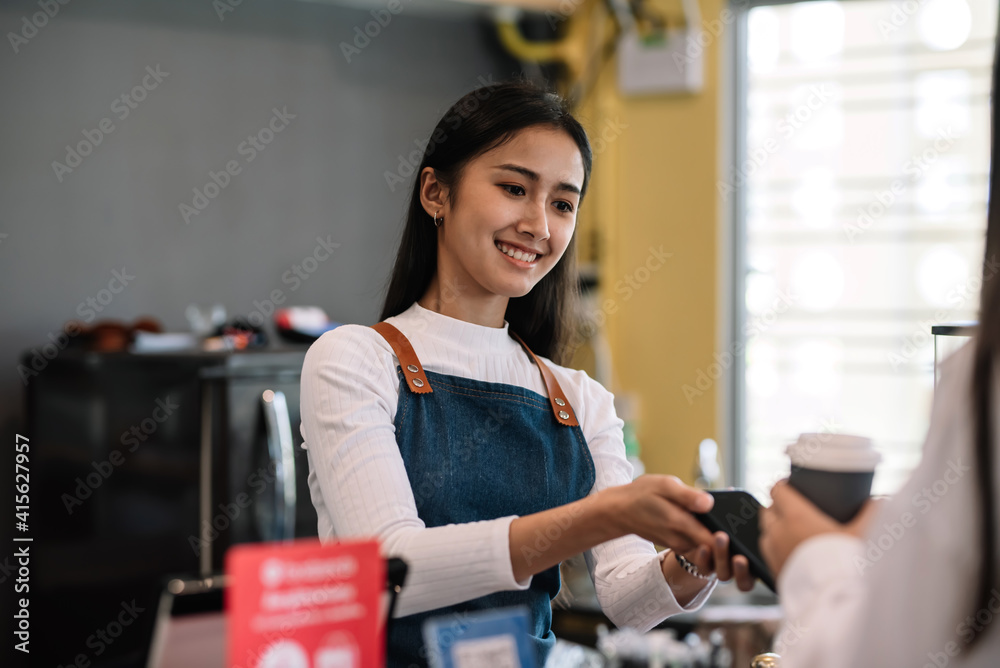Young Asian woman café entrepreneur provides service by mobile payment at coffee shop. Young Asian woman café entrepreneur provides service by mobile payment at coffee shop.