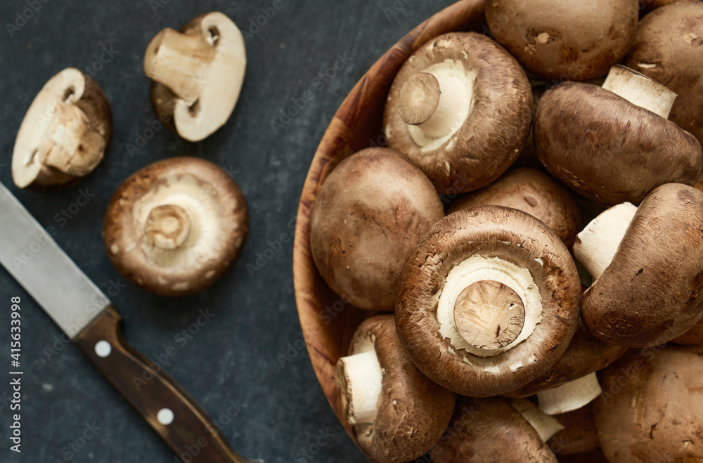Fresh champignon mushrooms in a wooden bowl, closeup, top view, shallow depth of sharpness Fresh champignon mushrooms in a wooden bowl, closeup, top view, shallow depth of sharpness