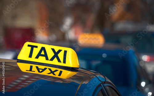 Taxi light sign or cab sign in yellow color on top of the car, blurred background. Taxi car sign on cab roof while parking on road waiting for passaenger. Taking safe rideshare during covid